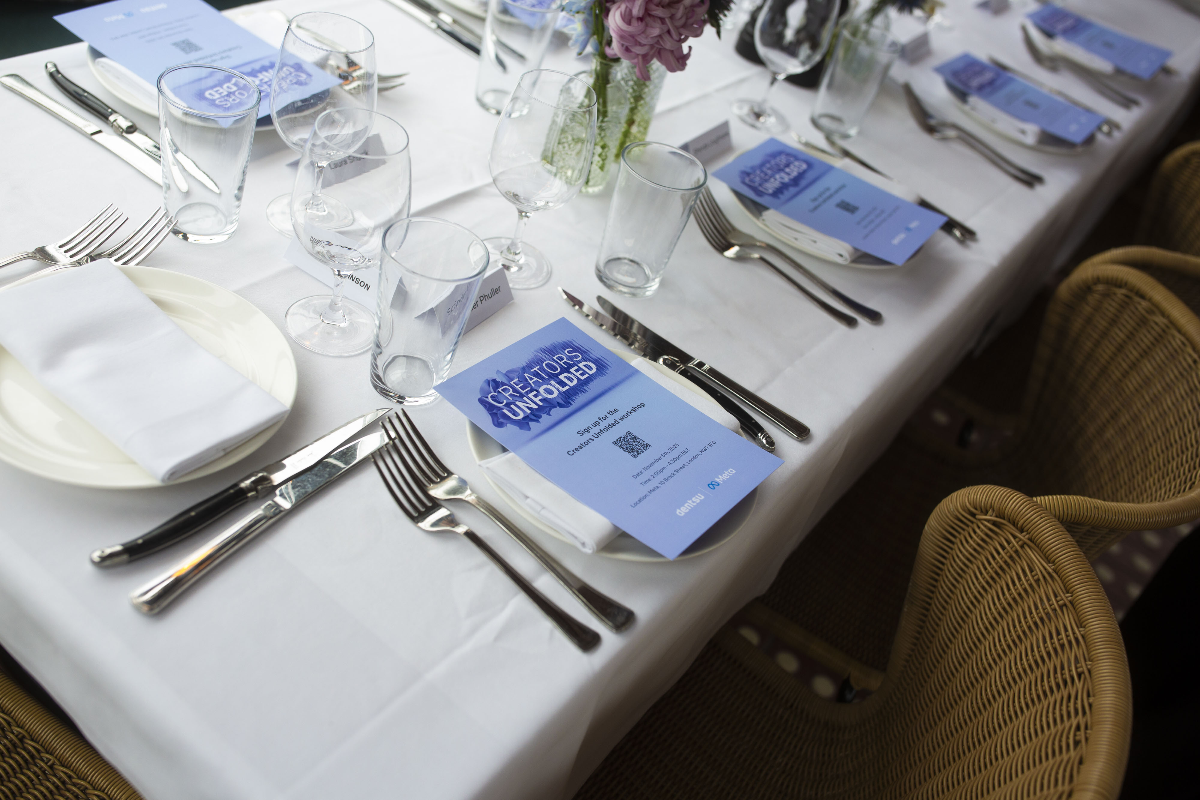 A neatly arranged dining table set for the dentsu x Meta “Creators Unfolded” event, featuring branded menus, glassware, and floral centrepieces prepared for guests